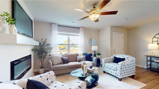 living room with a glass covered fireplace, baseboards, ceiling fan, and light wood finished floors