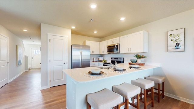 kitchen featuring light wood finished floors, appliances with stainless steel finishes, a breakfast bar, a peninsula, and light countertops