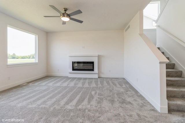 6918 SE 7th Ave, Pleasant Hill, IA 50327 - unfurnished living room with a glass covered fireplace, light carpet, a ceiling fan, and stairs
