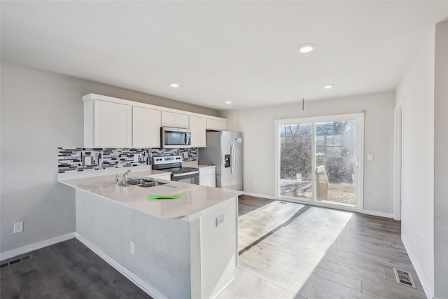 kitchen with stainless steel appliances, light hardwood / wood-style flooring, backsplash, kitchen peninsula, and white cabinets