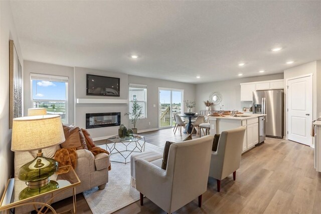 living room featuring a glass covered fireplace, light wood-style flooring, recessed lighting, and baseboards