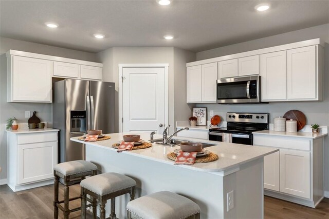 kitchen with wood finished floors, a breakfast bar, a sink, stainless steel appliances, and light countertops