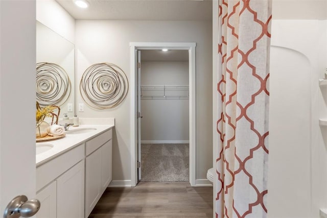 bathroom featuring curtained shower, baseboards, double vanity, wood finished floors, and a sink