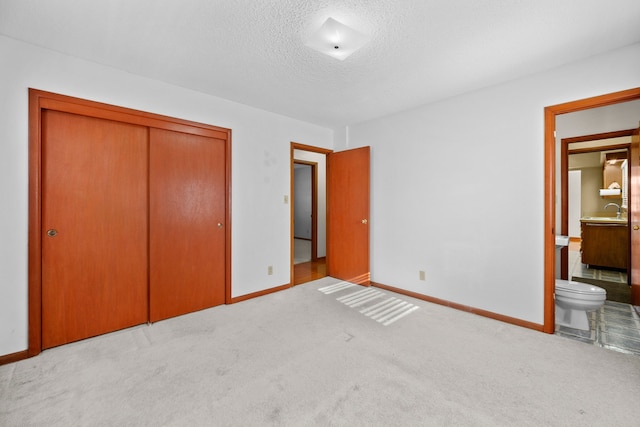 unfurnished bedroom featuring connected bathroom, a closet, light colored carpet, and a textured ceiling