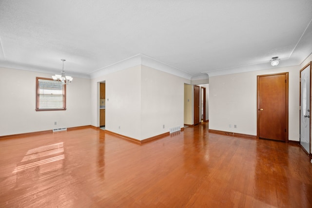 empty room featuring ornamental molding, a notable chandelier, and hardwood / wood-style floors