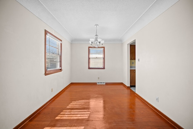 unfurnished room with hardwood / wood-style floors, ornamental molding, a textured ceiling, and an inviting chandelier