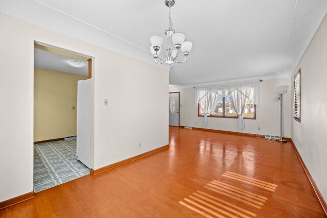 empty room featuring wood-type flooring and a chandelier