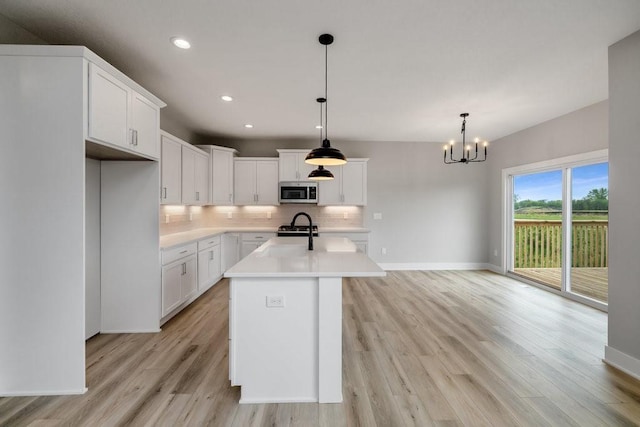 kitchen featuring a center island with sink, light hardwood / wood-style flooring, a notable chandelier, white cabinets, and hanging light fixtures