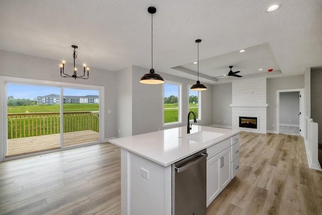 kitchen with dishwasher, a kitchen island with sink, a raised ceiling, sink, and white cabinetry