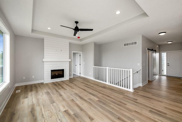 unfurnished living room with a tray ceiling, ceiling fan, a large fireplace, and light wood-type flooring