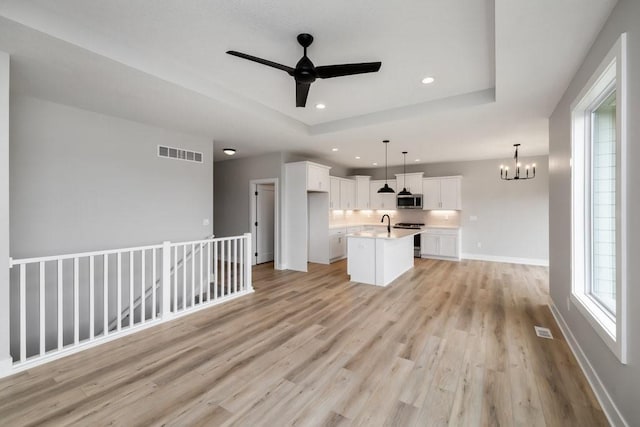 kitchen featuring stainless steel appliances, a healthy amount of sunlight, pendant lighting, a center island with sink, and white cabinets