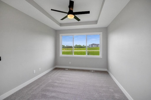 spare room with a tray ceiling, ceiling fan, and carpet