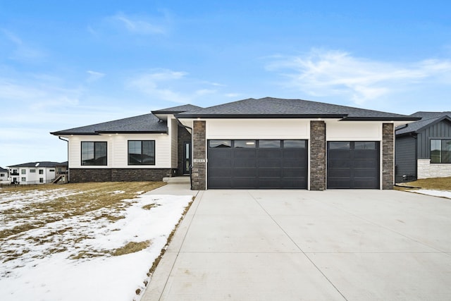 prairie-style home with a garage, driveway, a shingled roof, and stone siding