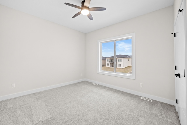 carpeted spare room with visible vents, ceiling fan, and baseboards