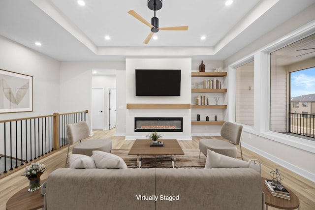 living room with a raised ceiling, ceiling fan, and light wood-type flooring