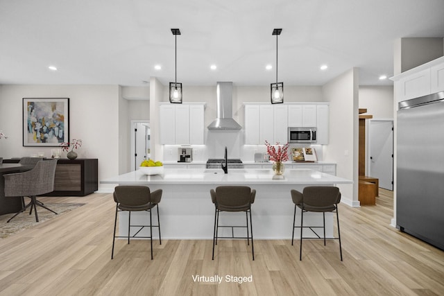 kitchen with decorative light fixtures, white cabinetry, a large island, stainless steel appliances, and wall chimney range hood