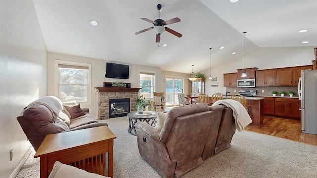 living room with vaulted ceiling, a stone fireplace, ceiling fan, and plenty of natural light