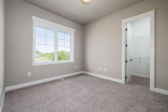 unfurnished bedroom with a walk in closet, a closet, and carpet floors