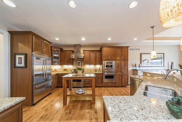 kitchen with light stone countertops, wall chimney exhaust hood, pendant lighting, stainless steel appliances, and sink