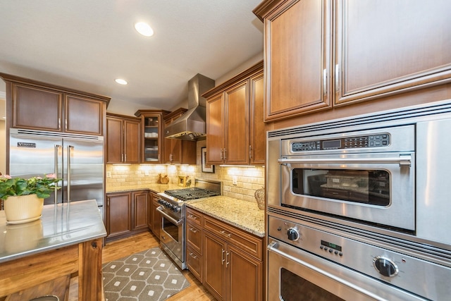 kitchen with light stone counters, tasteful backsplash, light hardwood / wood-style flooring, high end appliances, and wall chimney range hood