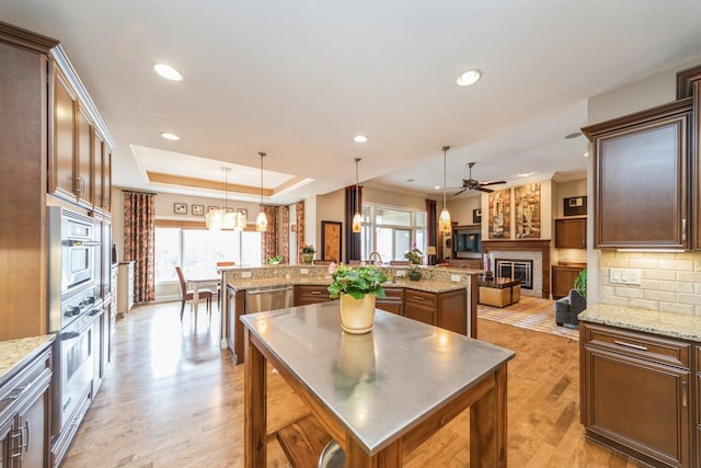 kitchen with a large island, pendant lighting, light hardwood / wood-style flooring, a tray ceiling, and appliances with stainless steel finishes