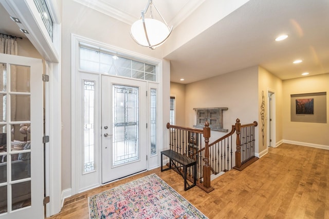 foyer entrance with light hardwood / wood-style floors, a wealth of natural light, and crown molding