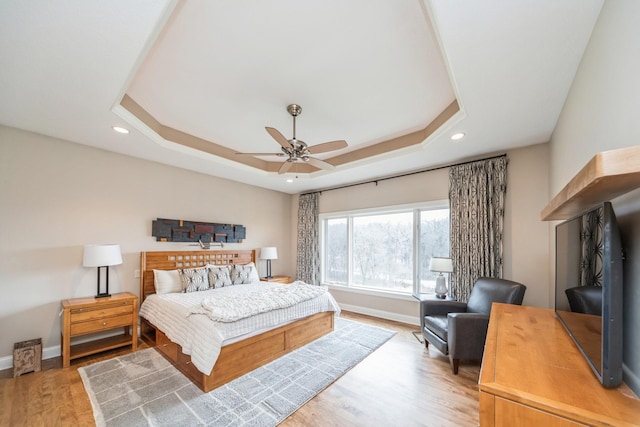 bedroom featuring ceiling fan, light hardwood / wood-style floors, and a tray ceiling