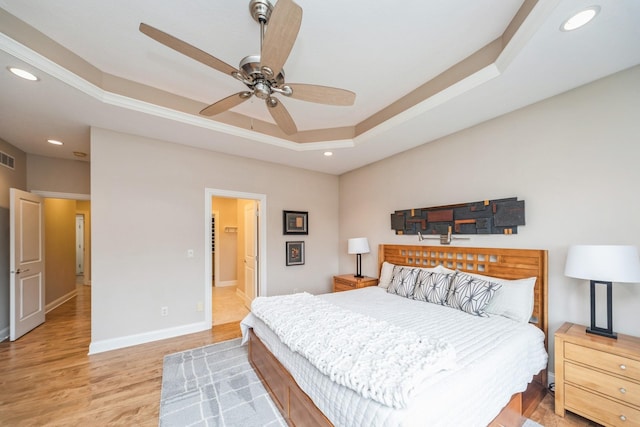 bedroom featuring light hardwood / wood-style floors, ceiling fan, a tray ceiling, and ornamental molding