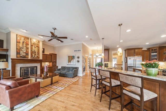 kitchen with built in fridge, decorative light fixtures, a kitchen bar, light stone countertops, and a stone fireplace