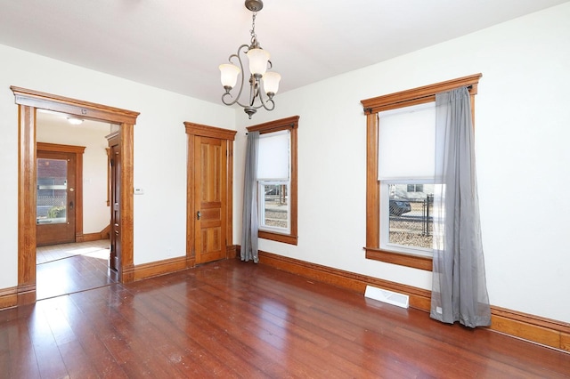 empty room featuring dark wood-type flooring and an inviting chandelier