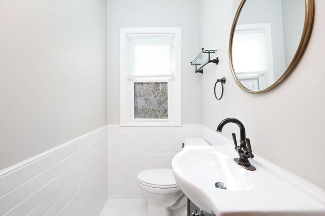 bathroom featuring toilet, tile walls, a healthy amount of sunlight, and sink