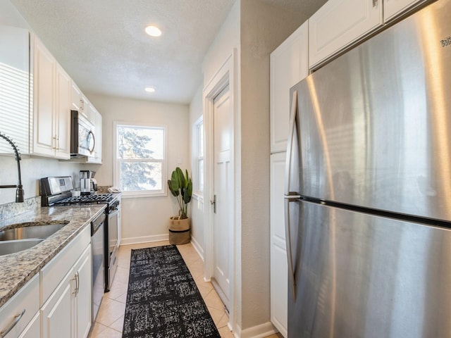 kitchen featuring appliances with stainless steel finishes, white cabinets, sink, light stone counters, and light tile patterned flooring