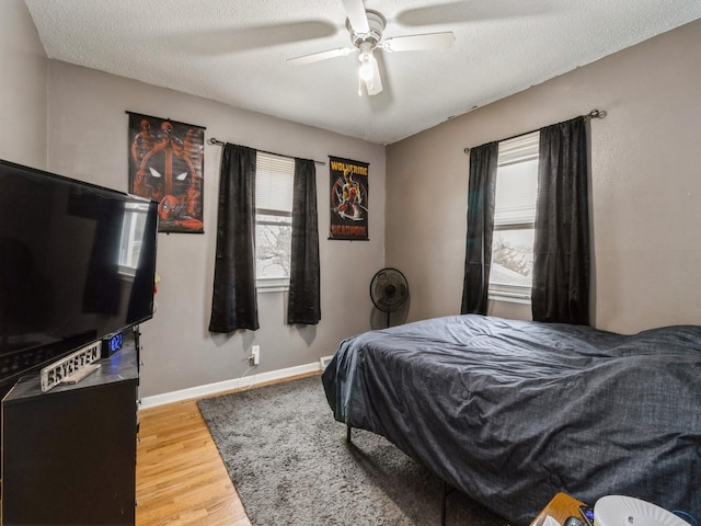 bedroom featuring ceiling fan, hardwood / wood-style floors, multiple windows, and a textured ceiling