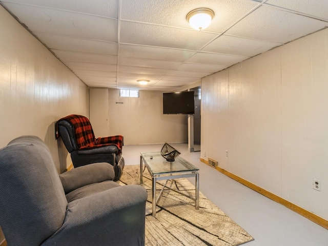 living room featuring a paneled ceiling, wood walls, and concrete flooring