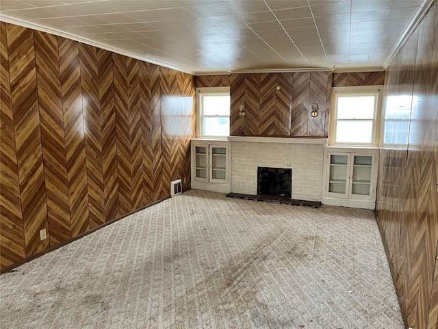 unfurnished living room with a brick fireplace, wooden walls, and crown molding