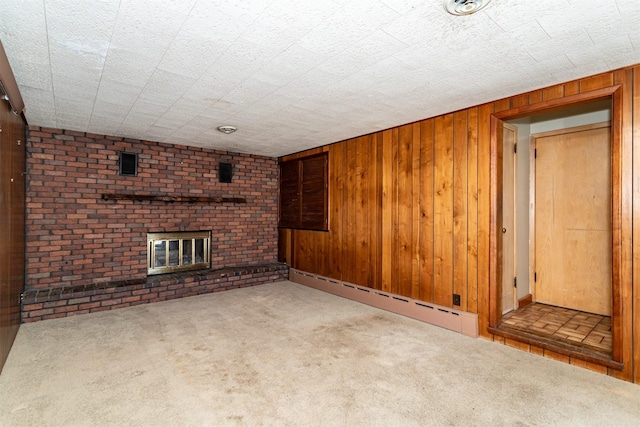 unfurnished living room with a brick fireplace, a baseboard radiator, carpet, and wooden walls