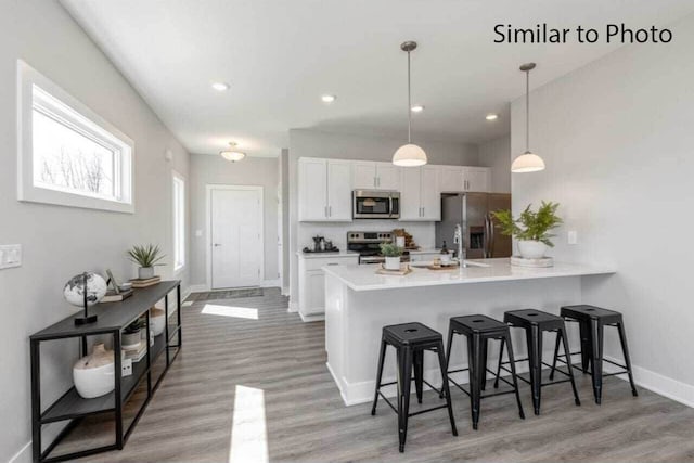 kitchen featuring light hardwood / wood-style flooring, decorative light fixtures, a breakfast bar area, white cabinets, and appliances with stainless steel finishes