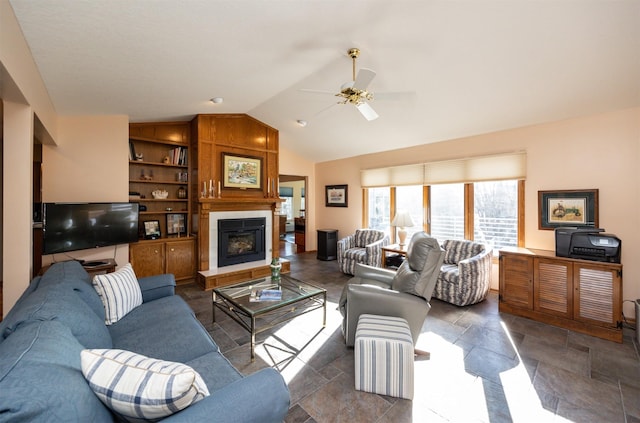 living room featuring a tiled fireplace, built in features, vaulted ceiling, and ceiling fan