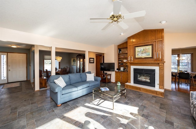 living room featuring ceiling fan with notable chandelier, a tiled fireplace, and lofted ceiling