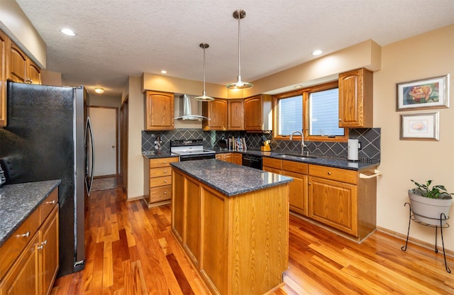 kitchen featuring sink, hanging light fixtures, a kitchen island, wall chimney range hood, and black appliances