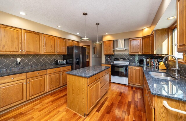 kitchen featuring electric range oven, sink, wall chimney exhaust hood, stainless steel fridge with ice dispenser, and a kitchen island