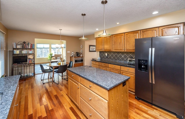 kitchen featuring hanging light fixtures, light wood-type flooring, a kitchen island, stainless steel refrigerator with ice dispenser, and backsplash