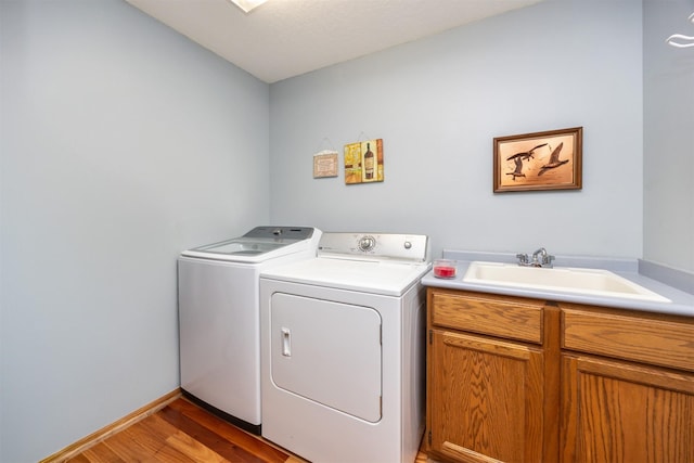 clothes washing area with cabinets, washing machine and clothes dryer, light hardwood / wood-style floors, and sink