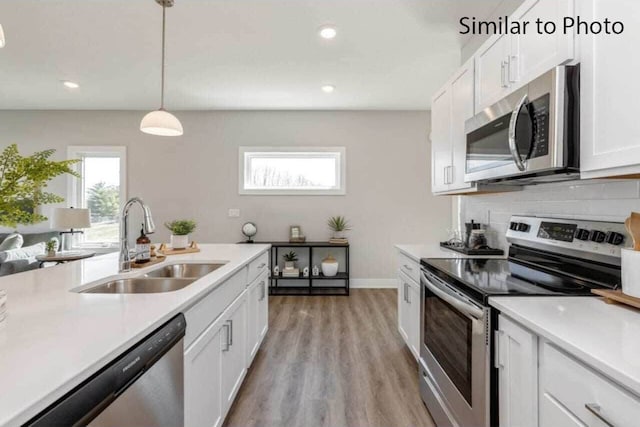 kitchen with stainless steel appliances, sink, decorative light fixtures, white cabinetry, and backsplash