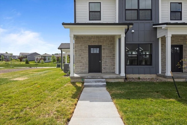 1991 S Warrior Ln, Waukee, IA 50263 - doorway to property featuring board and batten siding, central air condition unit, stone siding, and a lawn