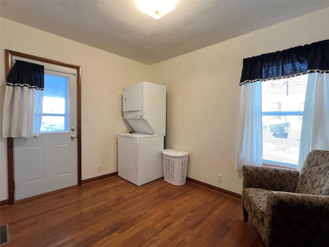 laundry room featuring stacked washer and clothes dryer, plenty of natural light, and wood-type flooring