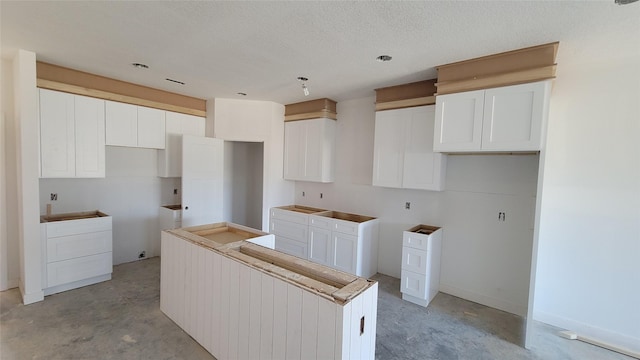 kitchen with white cabinets, a textured ceiling, a center island, and concrete flooring