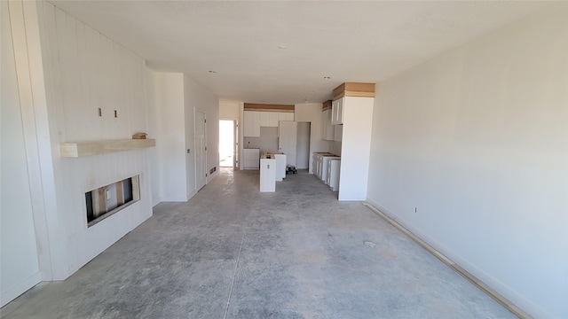 unfurnished living room with baseboards, washer / clothes dryer, a glass covered fireplace, and unfinished concrete floors