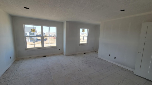 empty room featuring a healthy amount of sunlight, baseboards, and a textured ceiling