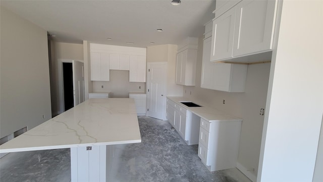 kitchen with a sink, light stone countertops, a kitchen island, and white cabinets